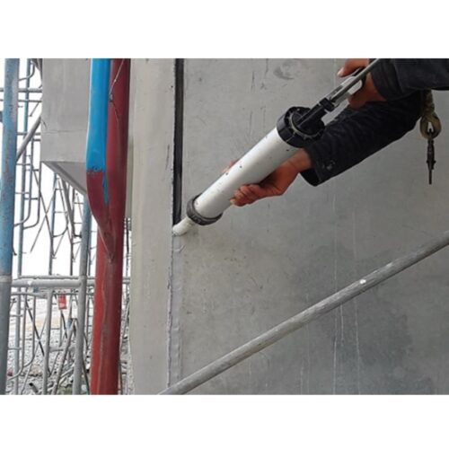 A person wearing work clothes is sealing the seams of precast wall blocks outdoors.