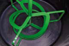 A green metal device with several loops and rods placed inside a black circular container.